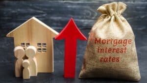 Model house, figures, and a bag labeled mortgage interest rates with an upward arrow.