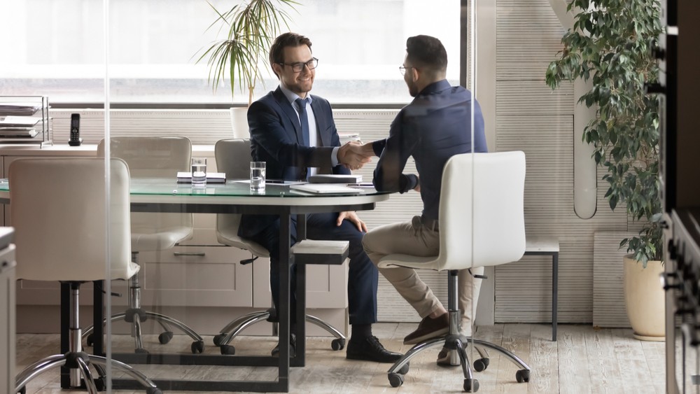 Smiling multiracial young businessmen handshake greeting get acquainted at boardroom briefing, excited diverse male business partners shake hands make agreement after successful office negotiations