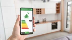 Person holding smartphone displaying energy efficiency app in modern kitchen.