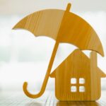 Model of umbrella with house on wooden table concept of the system of insurance savings and Housing insurance against impending loss and fire, building fire insurance concepts.