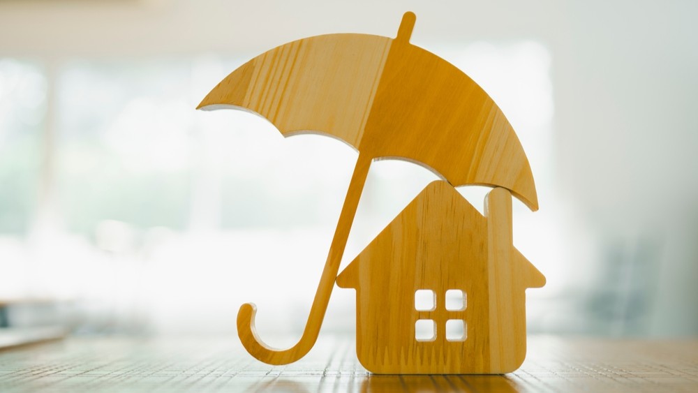 Model of umbrella with house on wooden table concept of the system of insurance savings and Housing insurance against impending loss and fire, building fire insurance concepts.