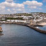 Aerial landscape of the quaint Cornish fishing town of Porthleven in Cornwall with rocky coastline and white sandy beach with harbour wall which is a popular tourist destination