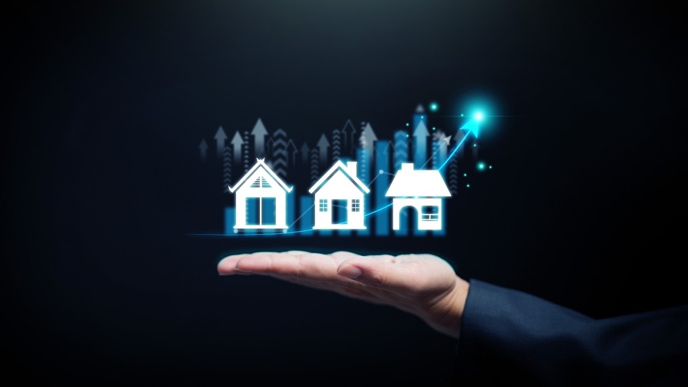 Real estate growth concept. Hand holds house icons and rising curve, symbolizing property investment, market expansion, and realestate development.