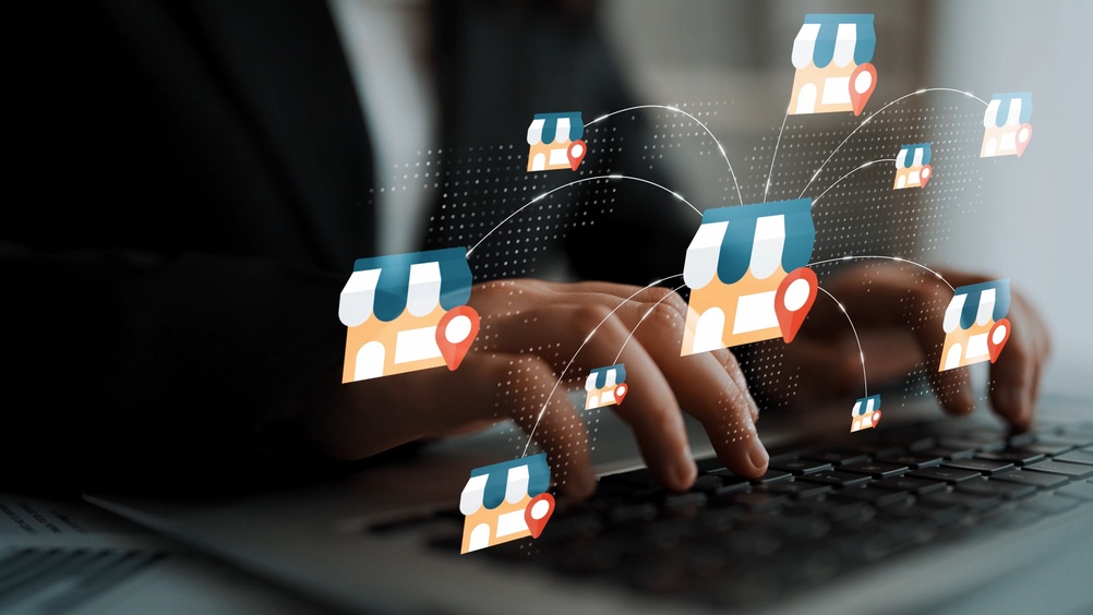 Hands typing on a keyboard with digital store icons and location markers representing online shopping and retail technology concepts Gluon.