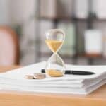 Hourglass, documents and coins on table in office