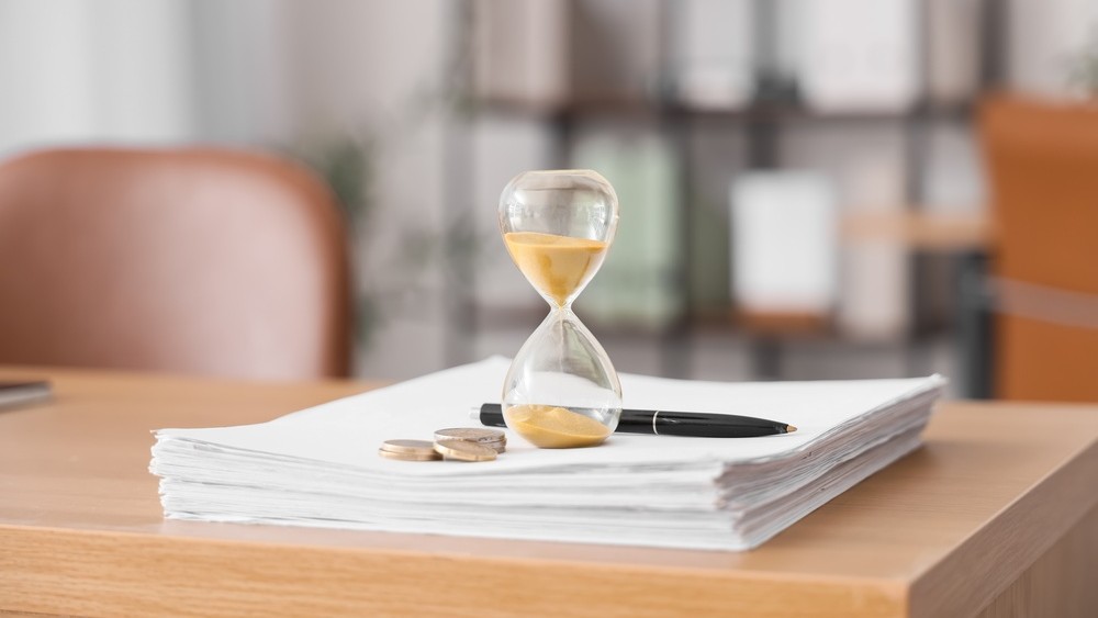 Hourglass, documents and coins on table in office