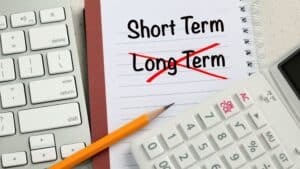 Notebook with 'Short Term' written and 'Long Term' crossed out, calculator, and pencil.