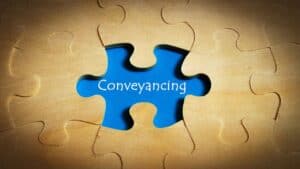 Blue puzzle piece with 'Conveyancing' text on wooden background.